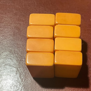 Puede incluir: Ocho fichas de juego rectangulares de color naranja est&aacute;n dispuestas en dos columnas. Las fichas tienen bordes redondeados y un acabado brillante. El fondo es una superficie marr&oacute;n oscuro.