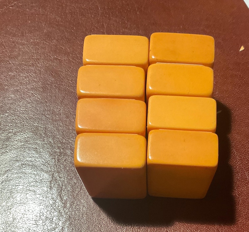 Puede incluir: Ocho fichas de juego rectangulares de color naranja est&aacute;n dispuestas en dos columnas. Las fichas tienen bordes redondeados y un acabado brillante. El fondo es una superficie marr&oacute;n oscuro.