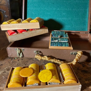 Pu&ograve; includere: Set di fiches da poker vintage in una custodia marrone. Il set include pile di fiches gialle, rosse e verdi. La custodia &egrave; aperta, rivelando la fodera in feltro verde e i porta fiches in legno.
