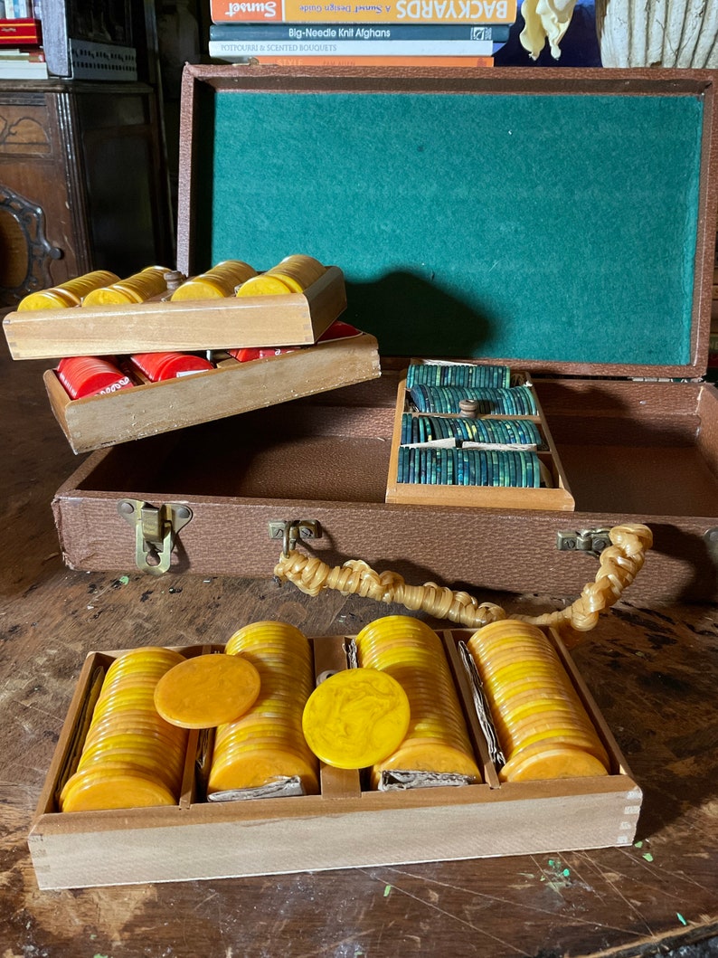 Pu&ograve; includere: Set di fiches da poker vintage in una custodia marrone. Il set include pile di fiches gialle, rosse e verdi. La custodia &egrave; aperta, rivelando la fodera in feltro verde e i porta fiches in legno.