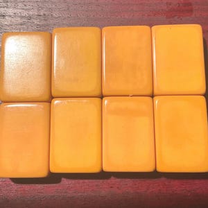 May include: Eight rectangular, amber-colored tiles arranged in two rows of four. The tiles have a smooth, glossy surface and are a warm, golden-yellow hue. The tiles are likely game pieces, possibly for a board game.