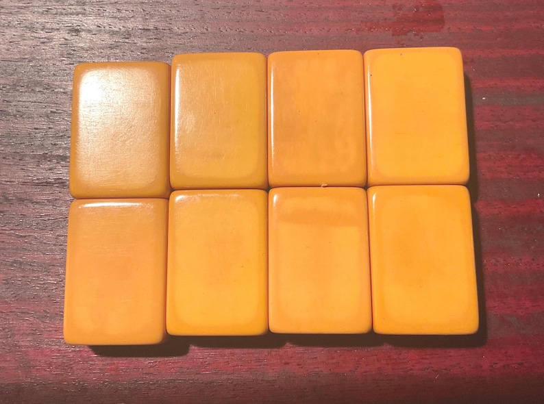 May include: Eight rectangular, amber-colored tiles arranged in two rows of four. The tiles have a smooth, glossy surface and are a warm, golden-yellow hue. The tiles are likely game pieces, possibly for a board game.