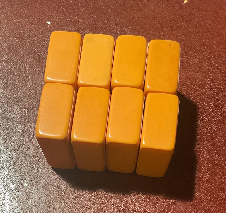 Puede incluir: Ocho baldosas rectangulares de color amarillo anaranjado dispuestas en dos filas de cuatro. Las baldosas tienen bordes redondeados y un acabado liso y brillante. El fondo es una superficie marr&oacute;n rojizo oscuro.