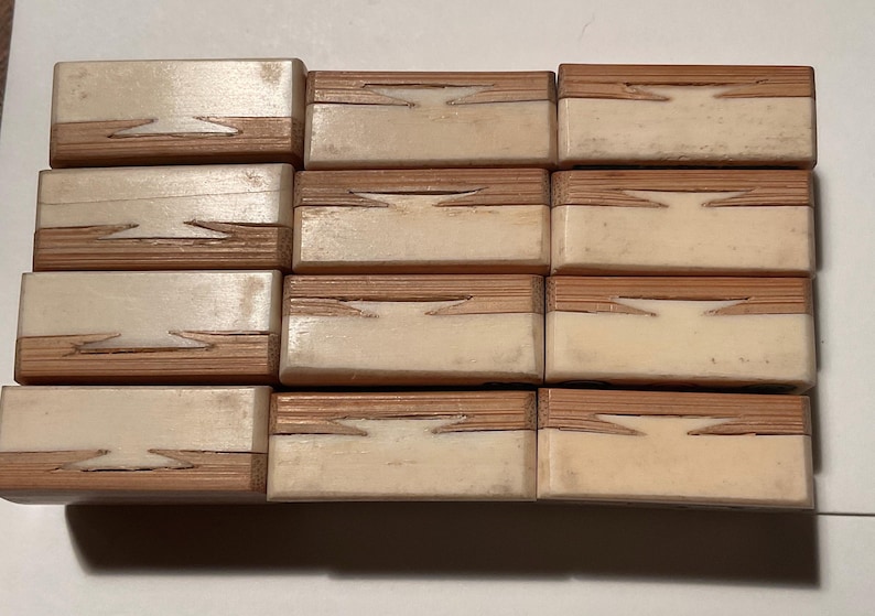May include: A collection of twelve rectangular blocks arranged in a grid, each featuring a two-tone design with a light cream-colored section and a natural wood-grain section joined by a distinct dovetail-style interlocking joint pattern.