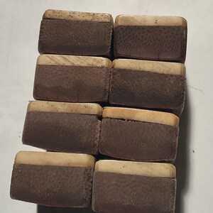 以下が含まれることがあります： ツートンカラーのデザインの、8つの小さな長方形の箱。蓋は薄いベージュ色で、箱の本体は暗い茶色で、表面はざらざらしています。箱は格子状に配置されています。