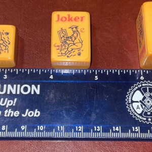 Puede incluir: Tres fichas de Mahjong amarillas vintage con texto "Joker" e ilustraciones. Una muestra un perro, otra un artista y la tercera est&aacute; en blanco. Una regla debajo mide en cent&iacute;metros.