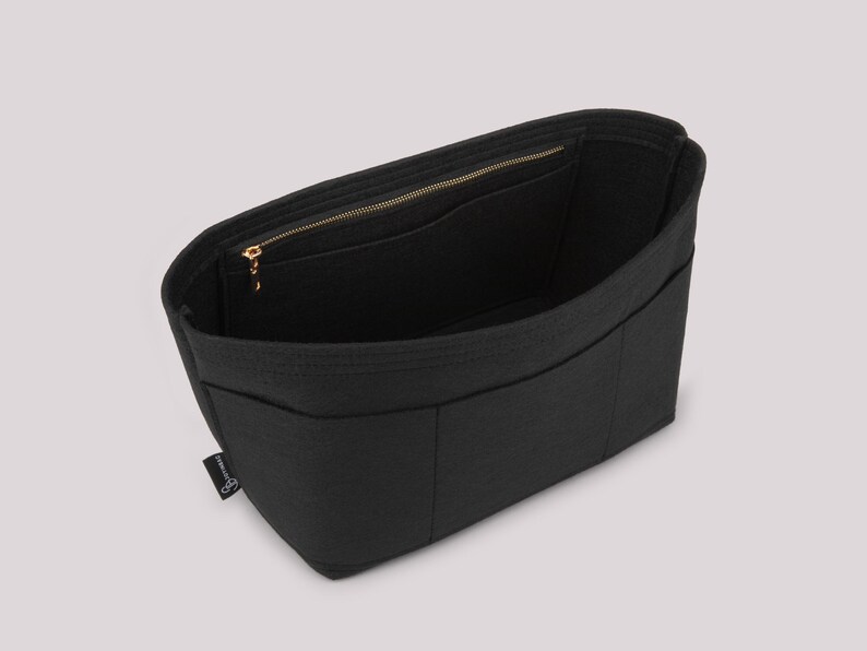 May include: Black felt bag organizer with multiple compartments and a zippered top closure. The interior features pockets for organization. The bag has a gold-colored zipper and a small label on the side.