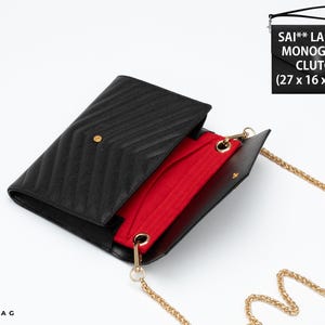 May include: A black chevron-quilted envelope clutch with a gold-tone chain strap and a vibrant red interior lining. The bag features a gold snap closure and measures 27 x 16 x 2 cm. The text SAI** LAUR*** MONOGRAM CLUTCH is visible in the corner.