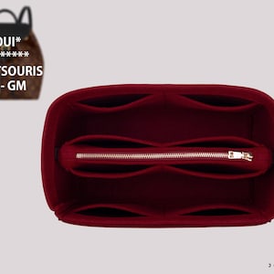 Peut inclure: Un organisateur de sac en feutre rouge profond doté de multiples compartiments intérieurs et d'une poche centrale zippée. L'insert est conçu pour un sac à dos à motif marron, étiqueté LOUI* VUI***** MONTSOURIS PM - GM, visible en haut à gauche.