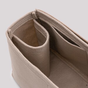 May include: Beige felt bag organizer with multiple compartments and pockets. The organizer is designed to fit inside a larger bag, helping to keep items organized.