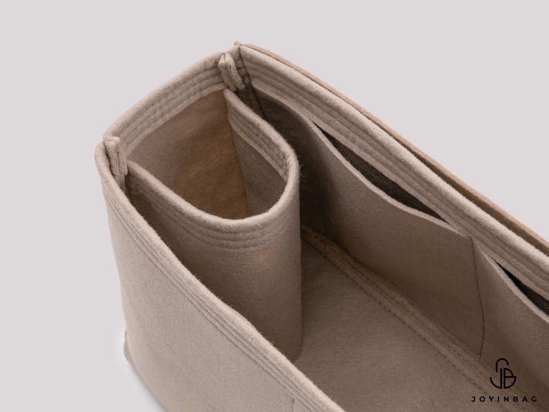 May include: Beige felt bag organizer with multiple compartments and pockets. The organizer is designed to fit inside a larger bag, helping to keep items organized.