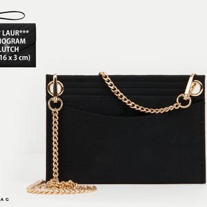 May include: A black rectangular felt bag organizer insert featuring a gold-tone metal chain strap attached with lobster clasps. The insert has multiple interior pockets and a smooth, structured design. Text in the image reads: SAI** LAUR*** MONOGRAM CLUTCH (21 x 16 x 3 cm).