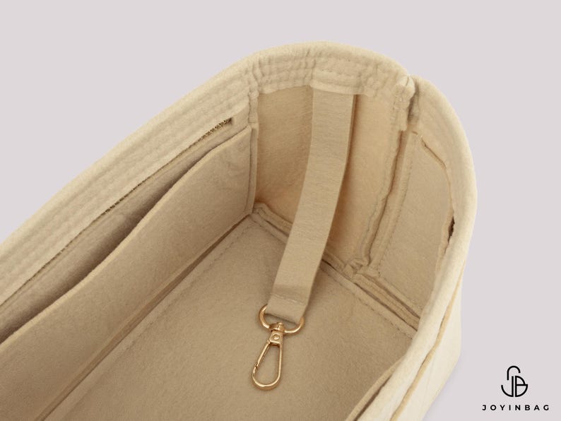 May include: Beige felt bag organizer with multiple pockets and a gold-colored clasp. The organizer has a structured design with a strap for easy handling. The interior features several compartments for storage.