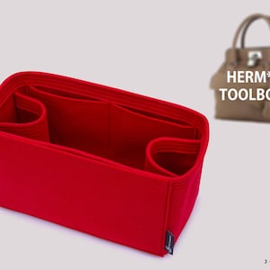 Könnte beinhalten: Ein leuchtend roter Handtaschen-Organizer aus Filz mit mehreren Innenfächern und abgerundeten Seitentaschen. Der Einsatz ist rechteckig und strukturiert gestaltet. Im Hintergrund ist eine beige Handtasche mit dem Text HERM** TOOLBOX zu sehen.