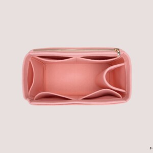 K&ouml;nnte beinhalten: Ein rosa Filztaschenorganizer mit mehreren F&auml;chern und einem Rei&szlig;verschluss. Der Organizer ist so konzipiert, dass er in eine gr&ouml;&szlig;ere Tasche passt und hilft, sie zu organisieren.