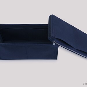 May include: A navy blue felt bag organizer with multiple compartments and a zippered top. The organizer is open and the top is folded back.