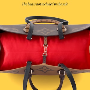 Puede incluir: Un bolso tote marrón y negro con forro rojo. El bolso tiene un patrón de monograma y dos asas superiores. El texto "The bag is not included in the sale" está impreso sobre el bolso.