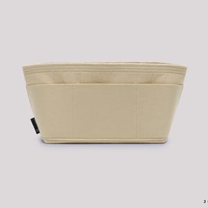 May include: A beige bag organizer with multiple compartments. The rectangular insert is made of a soft, felt-like material. The organizer has a structured shape with stitched seams and a small black tag on the side.