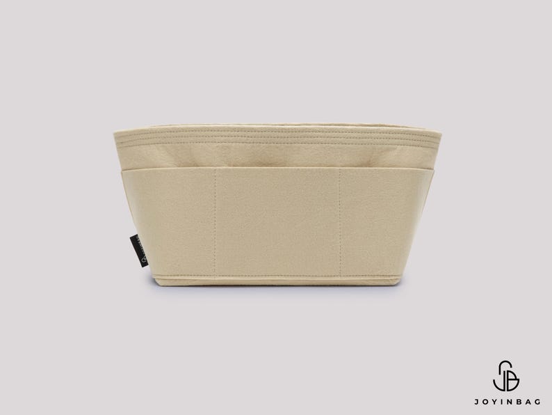 May include: A beige bag organizer with multiple compartments. The rectangular insert is made of a soft, felt-like material. The organizer has a structured shape with stitched seams and a small black tag on the side.