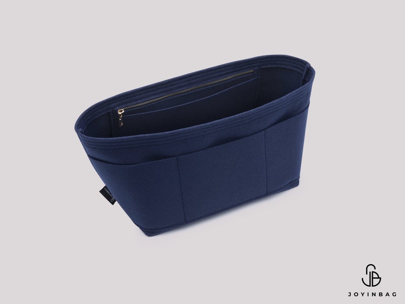May include: A navy blue felt bag organiser with multiple pockets and a zipped compartment. The organiser is designed to fit inside a larger bag and help keep it organised.