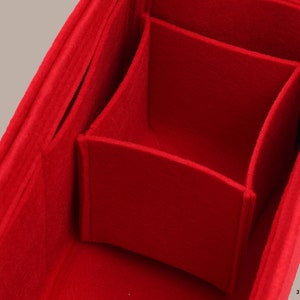 Puede incluir: Organizador de bolso de fieltro rojo con múltiples compartimentos. El organizador tiene una forma rectangular y está dividido en varias secciones. El fieltro es suave y mullido.
