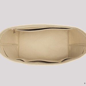 May include: Beige handbag organizer with multiple compartments and a zippered top pocket. The interior features several pockets for organization. The organizer is designed to fit inside a larger bag, providing structure and storage.