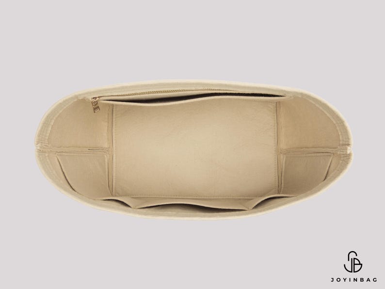 May include: Beige handbag organizer with multiple compartments and a zippered top pocket. The interior features several pockets for organization. The organizer is designed to fit inside a larger bag, providing structure and storage.