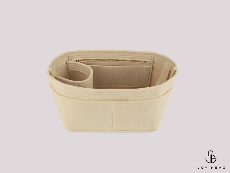 May include: Beige bag organizer with multiple compartments and a zippered pocket. The organizer is designed to fit inside a handbag, providing structure and organization. The product is made of a soft, felt-like material.