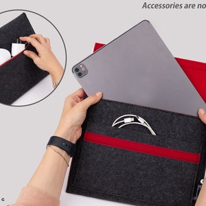 Può includere: Una custodia per laptop in feltro grigio con fodera in feltro rosso. La custodia ha una chiusura a zip e una piccola tasca sul davanti. La custodia è mostrata con un tablet e cavi di ricarica all'interno.