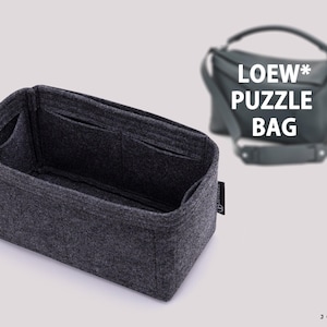 Op de afbeelding: Een donkergrijze vilten handtasorganizer met meerdere binnenzakken en een rechthoekige vorm. Op de achtergrond is een wazige donkergrijze handtas zichtbaar met de tekst LOEW* PUZZLE BAG in het wit gedrukt over de afbeelding van de tas.