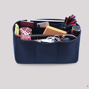 May include: A navy blue felt bag organizer with multiple compartments. The organizer is filled with various items, including a phone, wallet, sunglasses, and a water bottle.