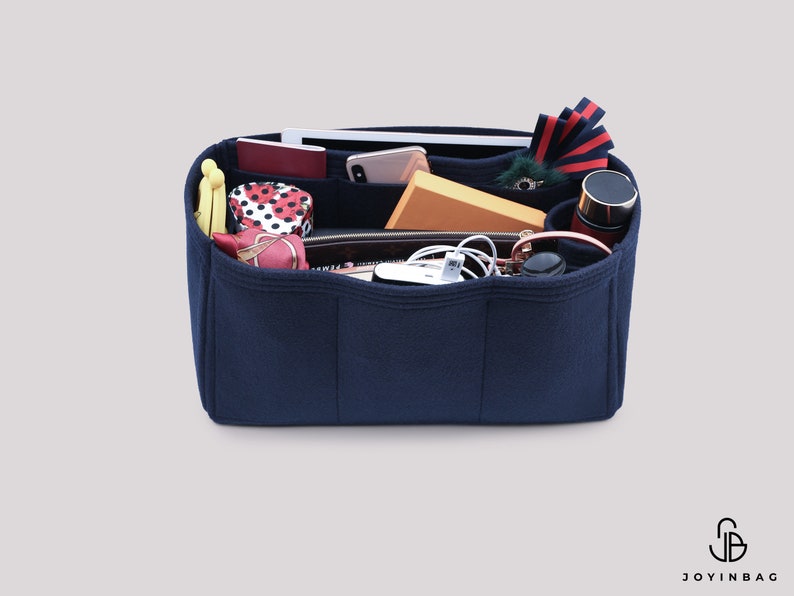 May include: A navy blue felt bag organizer with multiple compartments. The organizer is filled with various items, including a phone, wallet, sunglasses, and a water bottle.