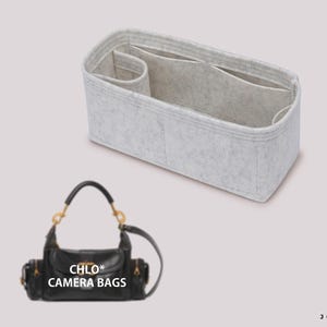 以下が含まれることがあります： 前面に「CHLO* CAMERA BAGS」の文字が書かれた、金色の金具が付いた黒い革製のカメラバッグ。バッグは、複数のコンパートメントが付いたグレーのフェルト製のバッグオーガナイザーの隣に置かれています。