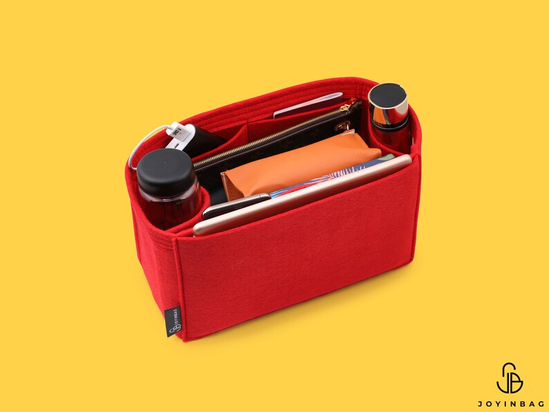 May include: Red felt handbag organizer with multiple compartments and pockets. The organizer is filled with various items, including a water bottle, phone, wallet, and a small cosmetic bag.