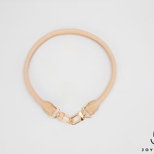 May include: A light tan leather bag handle with gold-coloured hardware. The handle is circular and has a clasp for easy attachment. The image is on a white background.