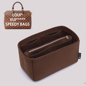 May include: A brown felt handbag organizer insert with multiple interior compartments and a central zippered pocket. In the background, a brown checkered handbag is visible with the text LOUI* VUI***** SPEEDY BAGS printed above it.