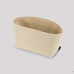 May include: Beige handbag organizer with multiple interior pockets. The rectangular organizer is made of a soft, light-colored fabric. The interior features several pockets for organization. A small black tag is attached to the side.
