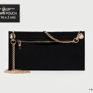 Puede incluir: Un organizador de fieltro negro con correa de cadena metálica dorada, un bolsillo horizontal con cremallera y un bolsillo abierto. El texto en la etiqueta dice SAI** LAUR*** UPTOWN POUCH (27 x 16 x 2 cm). Incluye herrajes de color dorado.