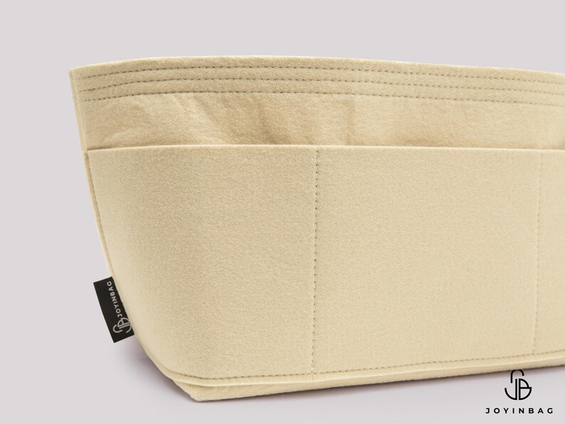 May include: Beige felt bag organizer with multiple compartments and stitched details. The organizer has a rectangular shape with a curved bottom and a small black tag with the text "JOYINBAG".