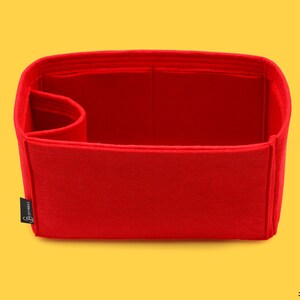 May include: Red felt bag insert with a single compartment and a small pocket on the side. The insert is designed to fit inside a handbag and help keep it organized.