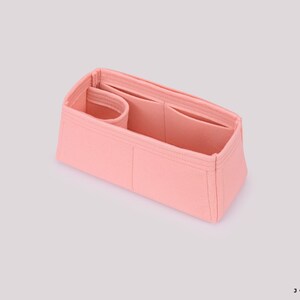 May include: A pink felt bag organizer with multiple compartments and pockets. The organizer is designed to fit inside a larger bag, helping to keep items organized.