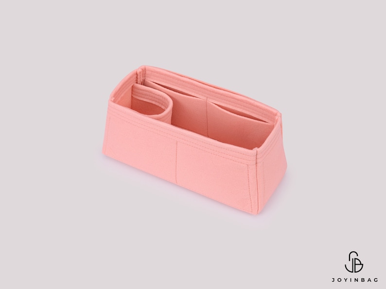 May include: A pink felt bag organizer with multiple compartments and pockets. The organizer is designed to fit inside a larger bag, helping to keep items organized.