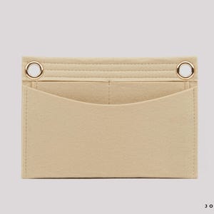 May include: A beige felt bag organizer insert featuring a rectangular shape with a curved front pocket, two internal compartments, and two gold-toned metal grommets at the top corners. The bottom right corner displays the black text JOYINBAG.