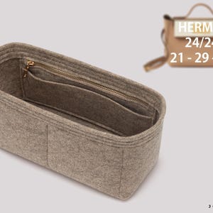 May include: A beige felt handbag organizer insert with rounded corners, featuring multiple interior compartments and a zippered pocket. A black tag with the white text JOYINBAG is attached to the side. A small tan handbag is visible in the background.