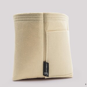 May include: A beige felt bag organizer with a rectangular shape and a small pocket on the side. The organizer has a stitched top and a black tag that reads "JOYINBAG". The bag is designed to help organize items inside a larger bag.