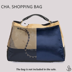 May include: A shopping bag with a black handle and a drawstring closure. The bag is divided into two sections: one in tan and the other in navy blue. The text "CHA. SHOPPING BAG" is at the top. The text "The bag is not included in the sale" is at the bottom.