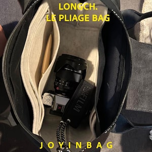 May include: A black Longch. Le Pliage bag with a beige felt organizer insert inside. The bag contains a silver and black Fujifilm camera with a lens and a black camera strap. The text LONGCH. LE PLIAGE BAG and JOYINBAG are visible.
