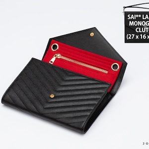 May include: A black envelope-style clutch organizer with a chevron-quilted exterior and a vibrant red interior lining. It features a gold-tone metal zipper, two circular metal eyelets, and a wrist strap. Text reads: SAI** LAUR*** MONOGRAM CLUTCH (27 x 16 x 2 cm).