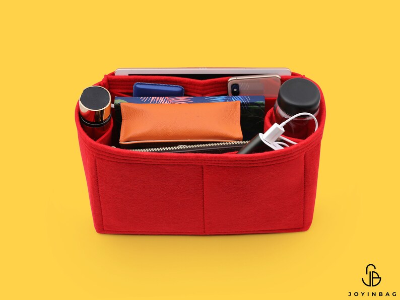 May include: Red felt bag organizer with multiple compartments. The organizer is filled with various items, including a phone, a water bottle, a power bank, and a notebook.