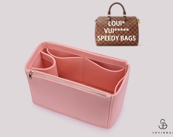 Puede incluir: Un organizador de bolso de fieltro rosa claro con múltiples compartimentos interiores y un bolsillo con cremallera en tono dorado. Al fondo, se ve un bolso a cuadros marrón con el texto LOUI* VUI***** SPEEDY BAGS impreso encima.